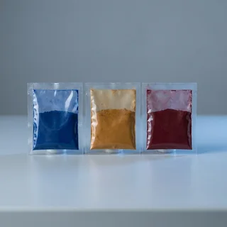 Três sachês monodose de pigmento em pó: azul, ocre e vermelho