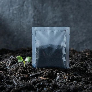 Sachê monodose de inoculante sobre solo escuro, com uma muda ao lado